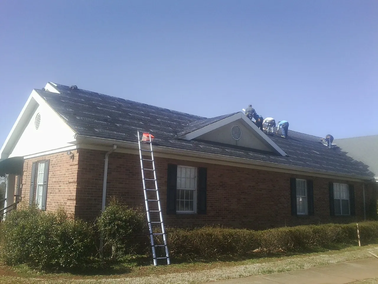 Crew tearing shingles off a brick ranch roof with a ladder set — Metal Roof Repair work by our crew in Pleasant Hall