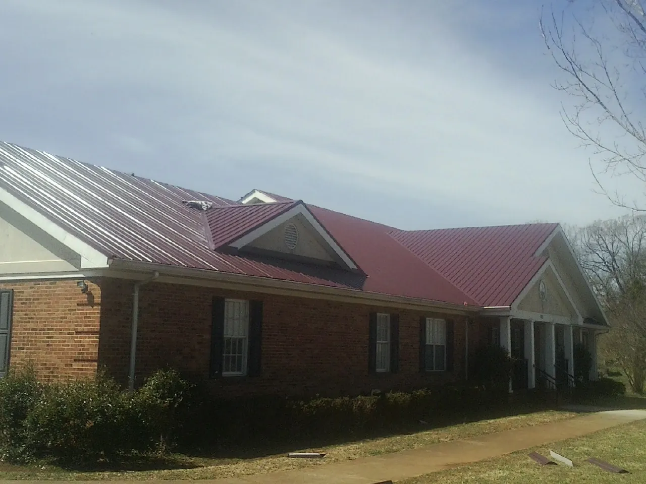 Red metal roof with gabled entries on a long brick building, from a Hail Damage Roof Repair job in Pleasant Hall