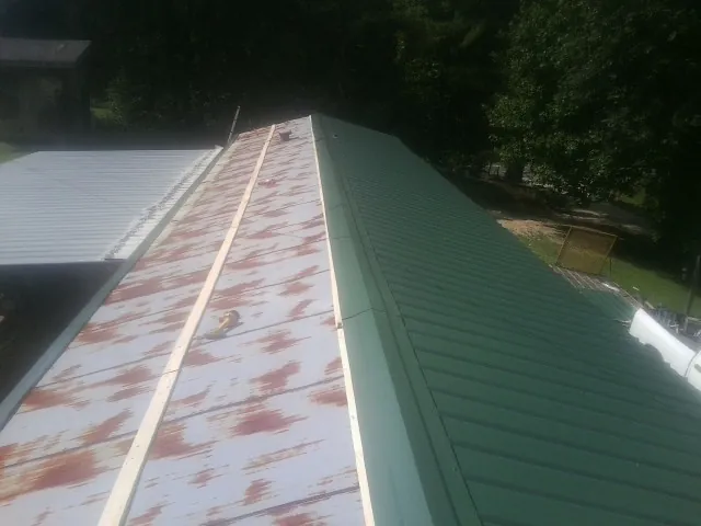Old rusted panels beside newly installed green metal roofing — Wind Damage Roof Repair by Roofing Brothers in Pleasant Hall