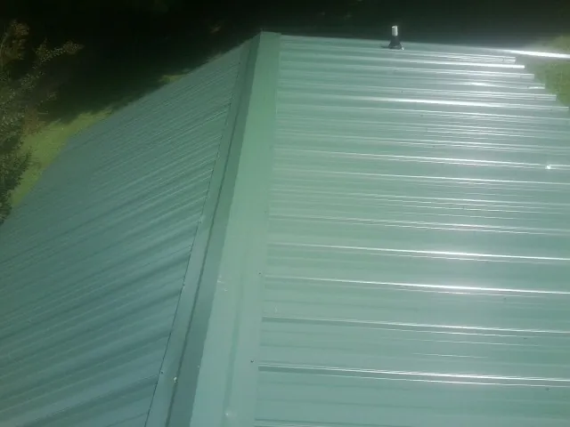 New green metal panels meeting at the ridge of a roof — Flat Roof Repair work by our crew in Pleasant Hall