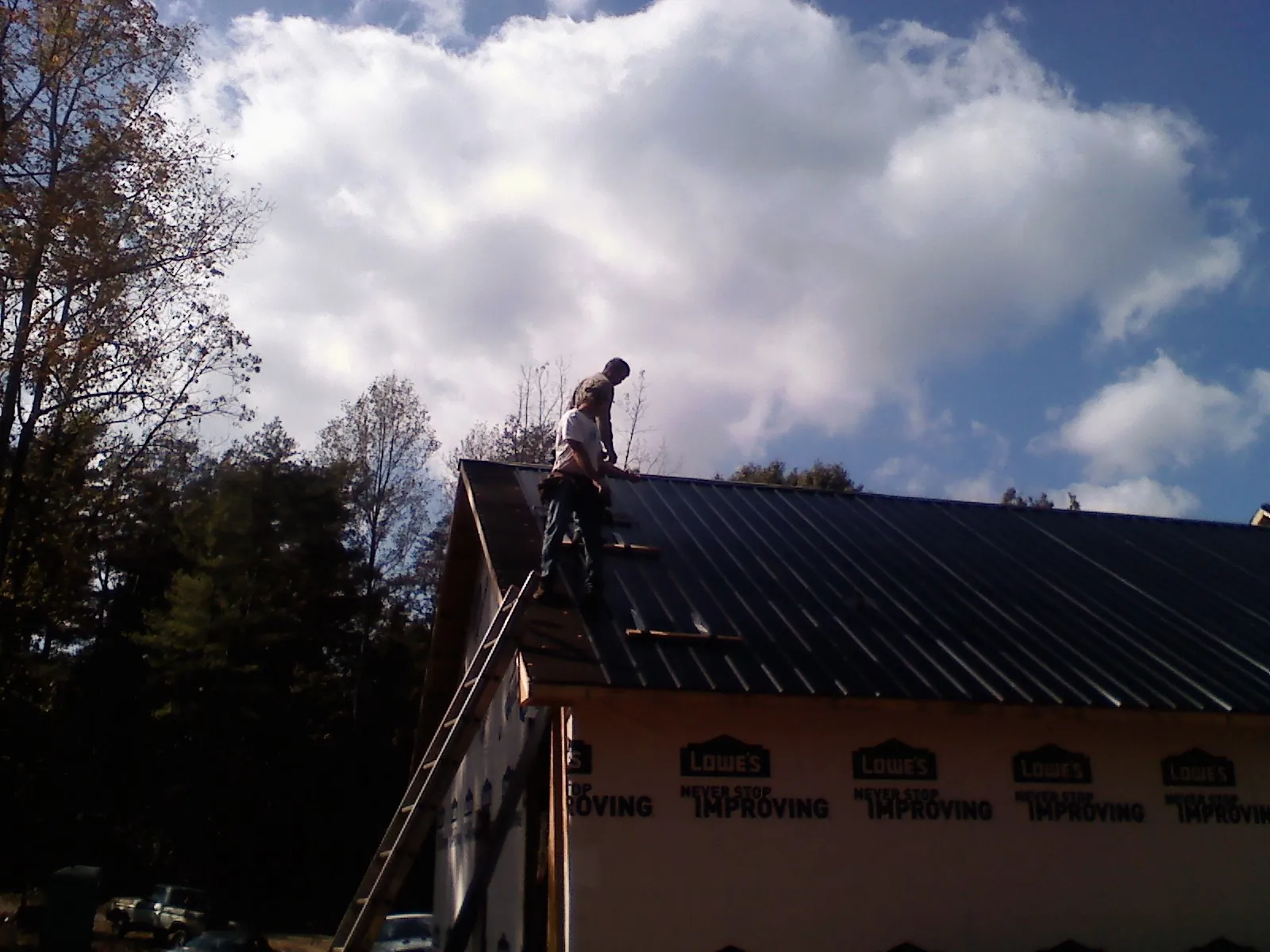 Roofer fastening dark metal panels high against a cloudy sky, from a Roof Inspection job in Pleasant Hall