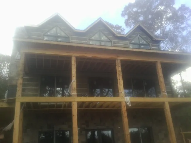 Dormers and porch framing on a large log home under construction — Roof Coating work by our crew in Pleasant Hall