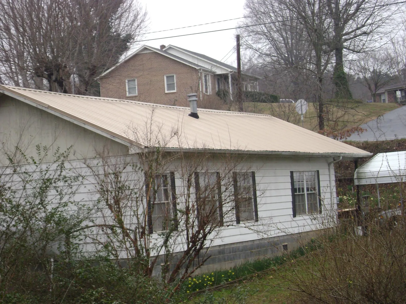 Tan metal roof on a white sided house set into a hillside — Commercial Roofing by Roofing Brothers in Pleasant Hall