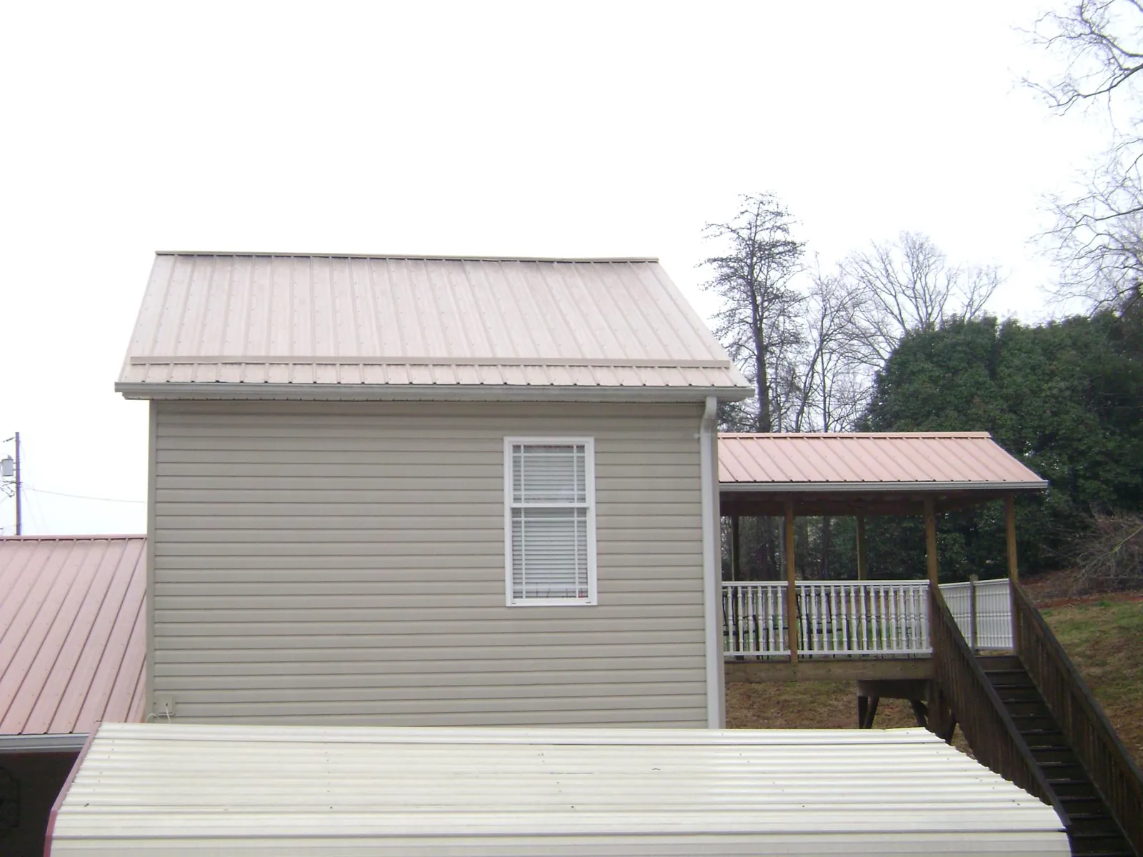 Tan metal roofs on a two story addition and attached porch, from a Roof Replacement job in Pleasant Hall